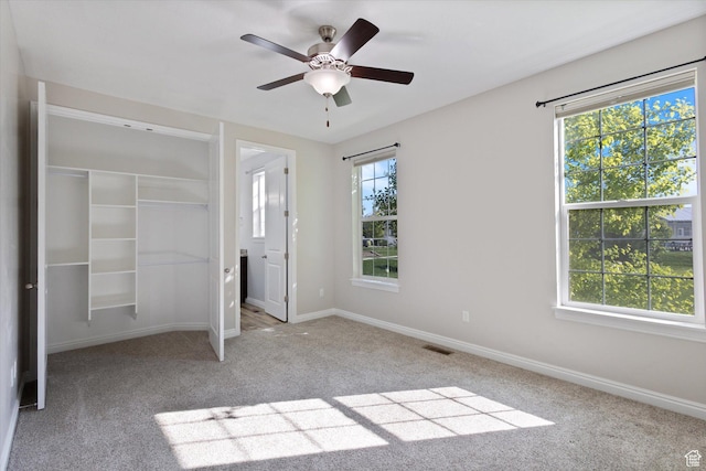 unfurnished bedroom featuring carpet floors, baseboards, a closet, a ceiling fan, and a spacious closet