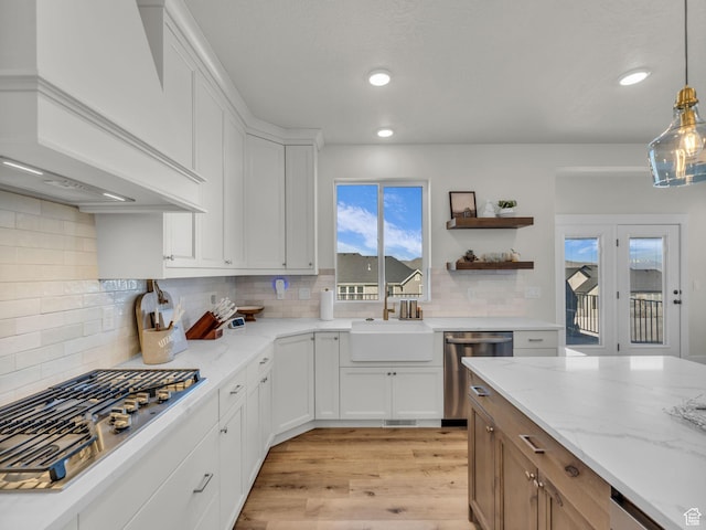 kitchen featuring premium range hood, stainless steel appliances, a sink, light wood finished floors, and white cabinets