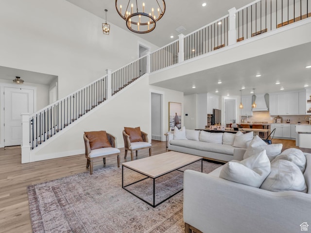 living area featuring a high ceiling, stairs, light wood-style flooring, a chandelier, and recessed lighting