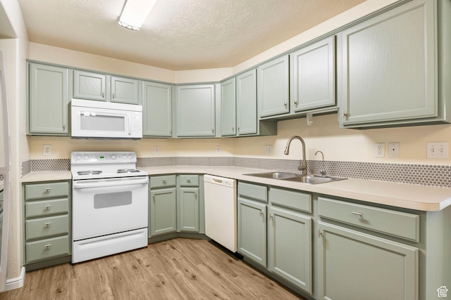 kitchen featuring white appliances, a sink, green cabinets, light wood-type flooring, and light countertops