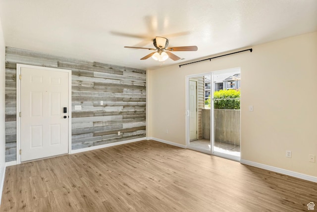 empty room featuring a ceiling fan, baseboards, wood finished floors, an accent wall, and wooden walls