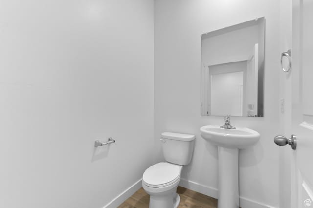 half bath with wood finished floors, baseboards, and toilet