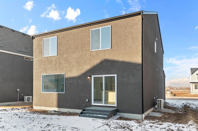 snow covered house featuring a cooling unit and stucco siding