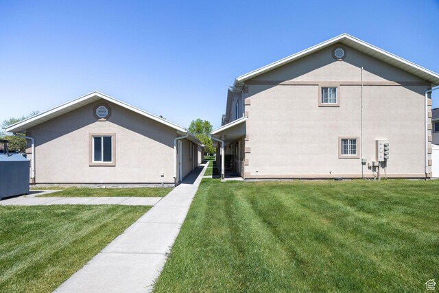 rear view of property featuring a lawn and stucco siding