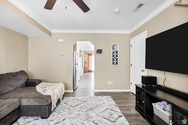 living room with arched walkways, crown molding, a ceiling fan, baseboards, and wood finished floors