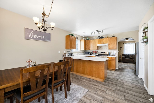 kitchen featuring under cabinet range hood, appliances with stainless steel finishes, a chandelier, a peninsula, and light countertops