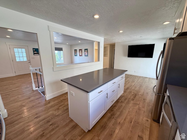 9977 S Lannae Dr E, Sandy, UT 84094 - kitchen featuring a textured ceiling, white cabinets, dark countertops, wood finished floors, and a center island