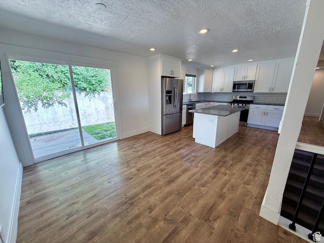 9977 S Lannae Dr E, Sandy, UT 84094 - kitchen with stainless steel appliances, white cabinetry, a textured ceiling, backsplash, and wood finished floors