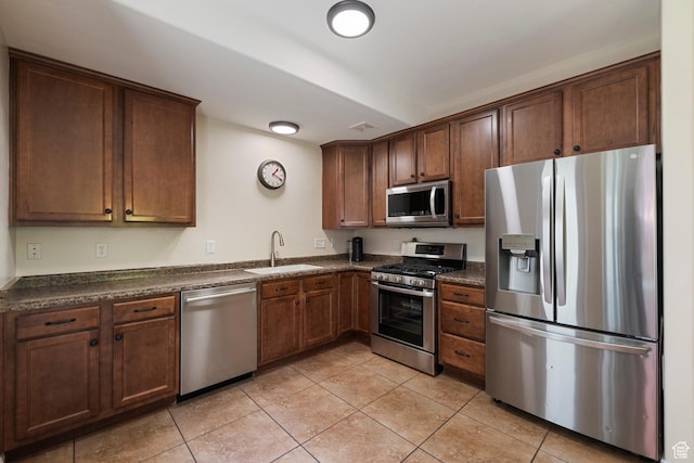 kitchen with appliances with stainless steel finishes, a sink, dark countertops, and light tile patterned flooring