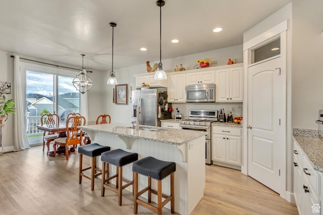 14397 S Hill Shadow Way Unit 87, Herriman, UT 84096 - kitchen with appliances with stainless steel finishes, light wood-style floors, a breakfast bar area, white cabinets, and a center island with sink