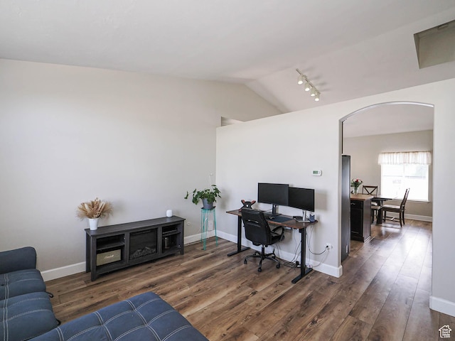 home office with arched walkways, vaulted ceiling, wood finished floors, rail lighting, and baseboards