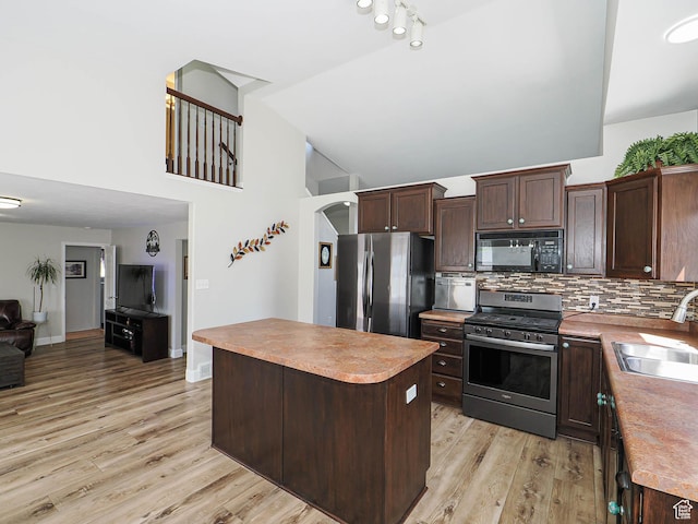 kitchen featuring stainless steel appliances, a sink, light wood-style flooring, dark brown cabinets, and high vaulted ceiling