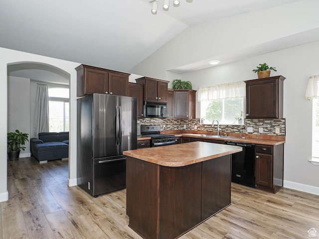 kitchen featuring black appliances, a sink, arched walkways, dark brown cabinetry, and a center island