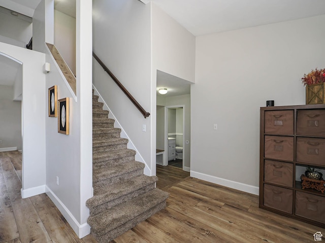 stairway featuring wood finished floors, baseboards, and arched walkways