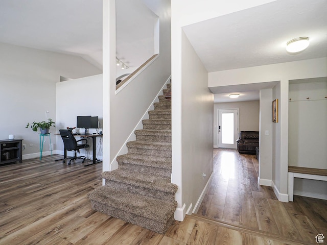 stairway featuring wood finished floors, baseboards, and lofted ceiling