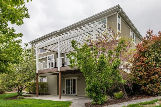 rear view of house with stucco siding, a pergola, a patio, and a yard