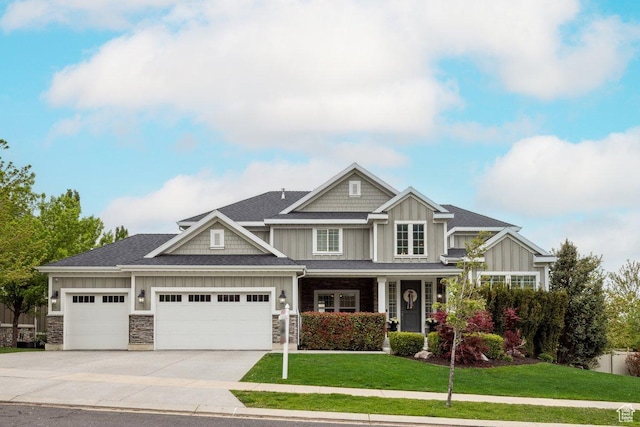 craftsman-style house with board and batten siding, an attached garage, a front lawn, concrete driveway, and stone siding
