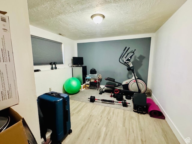 workout area with wood finished floors, a textured ceiling, and baseboards