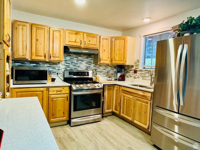 kitchen with stainless steel appliances, under cabinet range hood, light countertops, and a sink