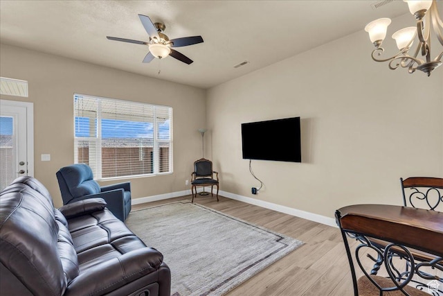 living area featuring light wood-style flooring, a chandelier, ceiling fan, and baseboards
