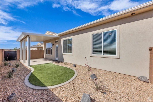 rear view of house with a patio area, fence, and stucco siding