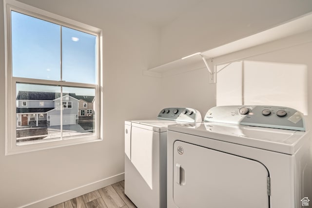 clothes washing area featuring washing machine and dryer, light wood-style floors, and baseboards