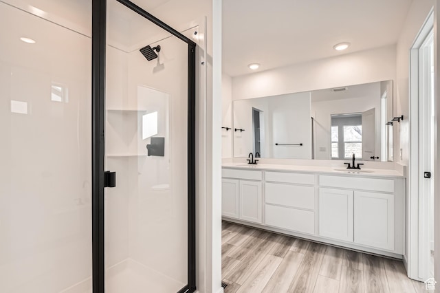 bathroom featuring a stall shower, double vanity, and wood finished floors