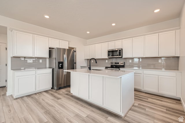 kitchen with stainless steel appliances, a sink, backsplash, light countertops, and white cabinets