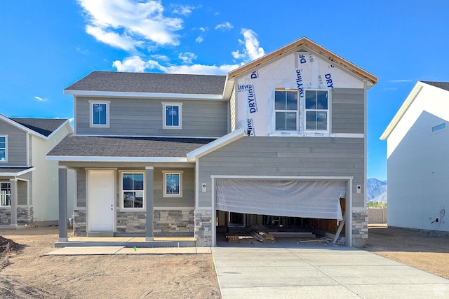 view of front facade featuring driveway, stone siding, an attached garage, covered porch, and roof with shingles
