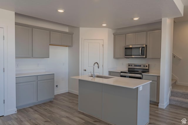 kitchen featuring stainless steel appliances, a sink, gray cabinets, light wood finished floors, and an island with sink