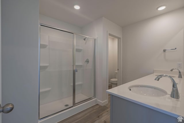 bathroom with wood finished floors, a stall shower, toilet, double vanity, and recessed lighting
