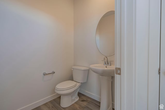 half bath with baseboards, toilet, wood finished floors, and a sink