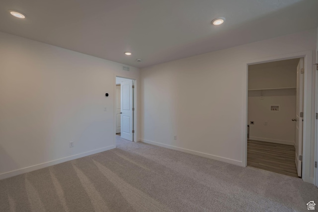 unfurnished bedroom featuring light colored carpet, recessed lighting, baseboards, a walk in closet, and a closet