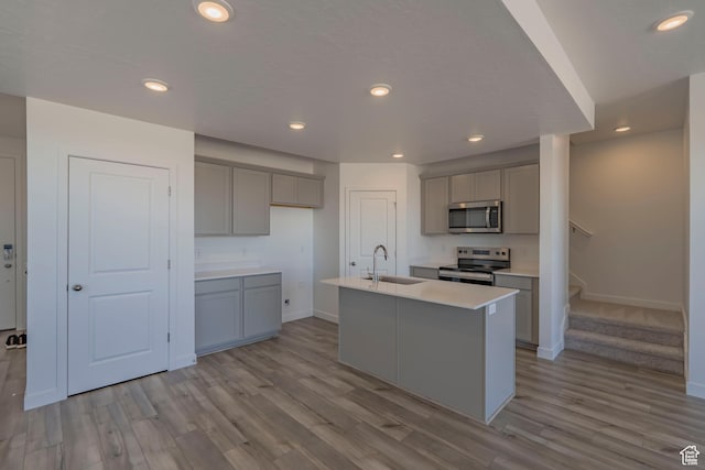 kitchen with appliances with stainless steel finishes, gray cabinetry, a sink, baseboards, and light wood-type flooring