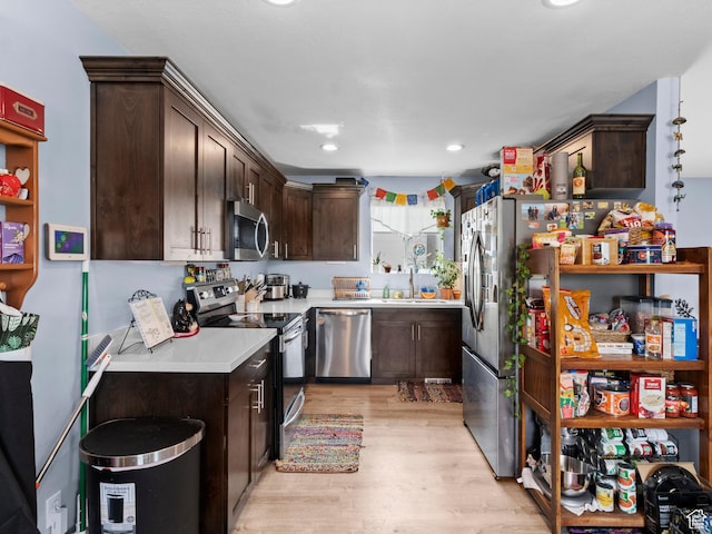 kitchen with appliances with stainless steel finishes, dark brown cabinets, light countertops, light wood-type flooring, and a sink