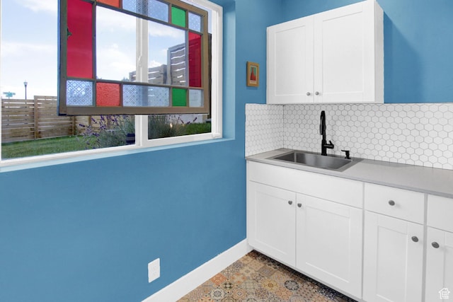 kitchen featuring a sink, decorative backsplash, baseboards, white cabinetry, and light countertops