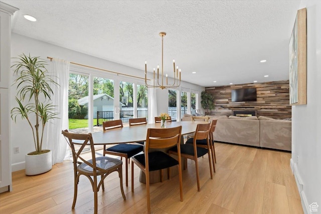 dining space featuring light wood-style flooring, recessed lighting, a textured ceiling, a chandelier, and a fireplace