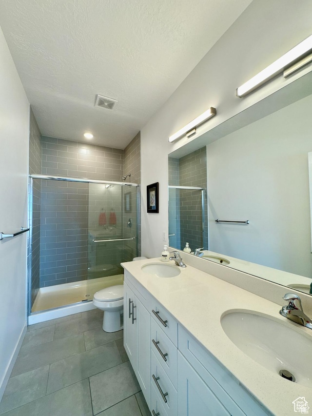 full bathroom featuring a stall shower, tile patterned floors, toilet, double vanity, and a textured ceiling