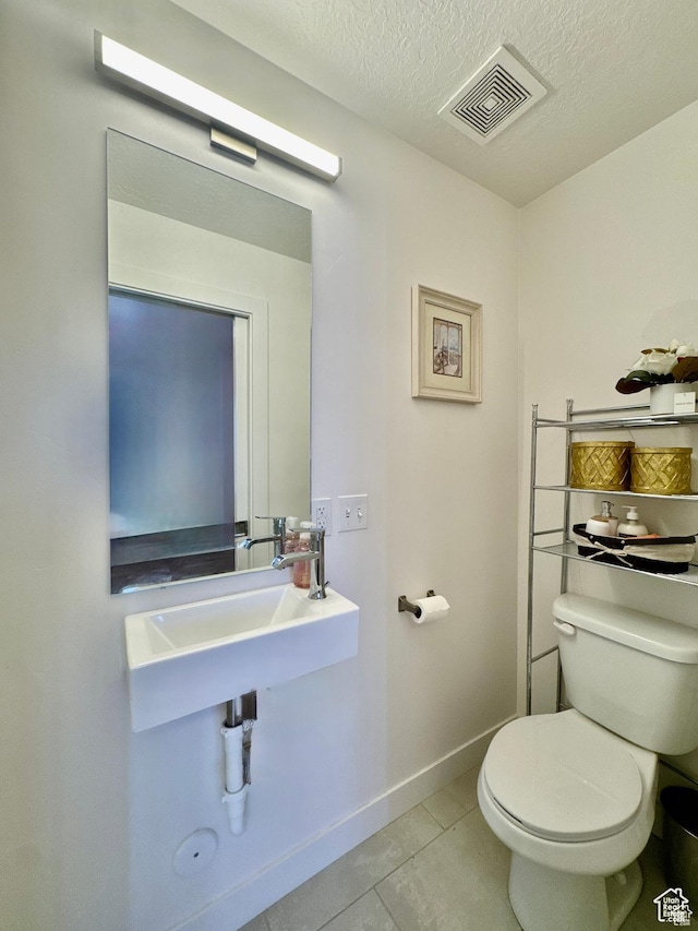 half bath with toilet, tile patterned floors, baseboards, a textured ceiling, and a sink