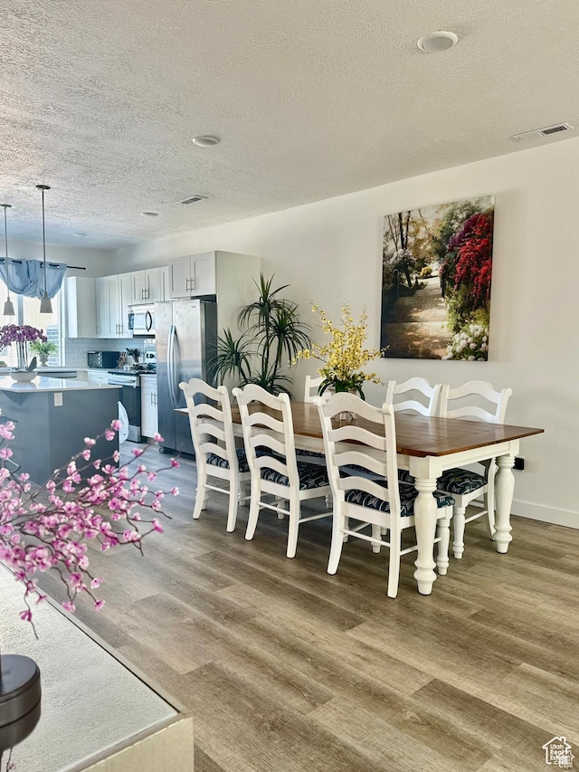 dining space featuring a textured ceiling, wood finished floors, and baseboards