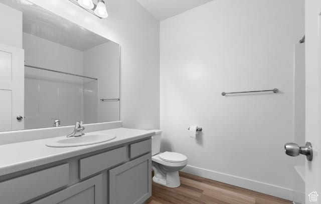 bathroom featuring wood finished floors, baseboards, toilet, vanity, and a shower