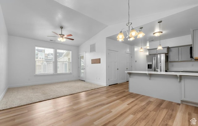 kitchen featuring stainless steel fridge, gray cabinets, a breakfast bar area, light countertops, and lofted ceiling