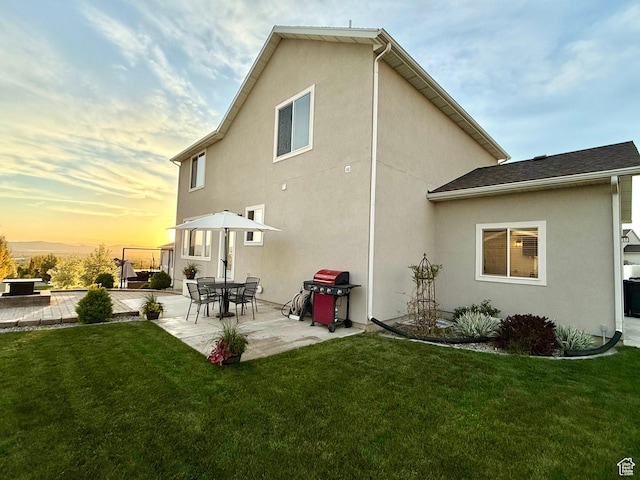 back of property at dusk with a patio area, a lawn, and stucco siding