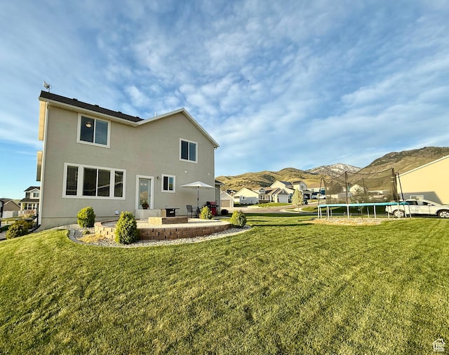 back of property with a patio, a lawn, a trampoline, and a mountain view