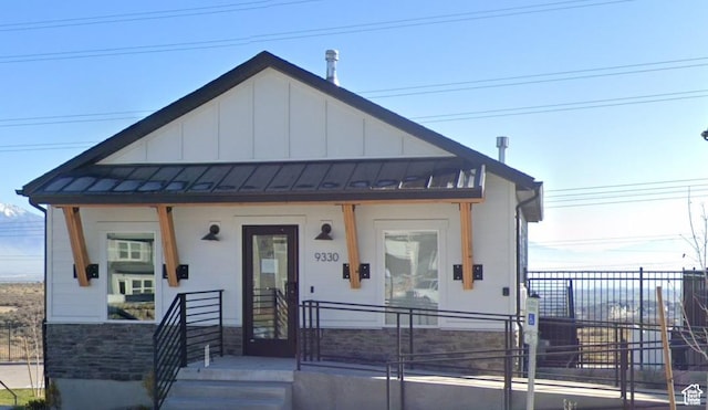 view of front of house featuring fence, board and batten siding, a standing seam roof, covered porch, and stone siding