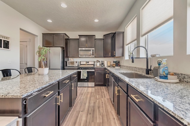 kitchen with stainless steel appliances, a sink, light wood-type flooring, a kitchen island, and a textured ceiling