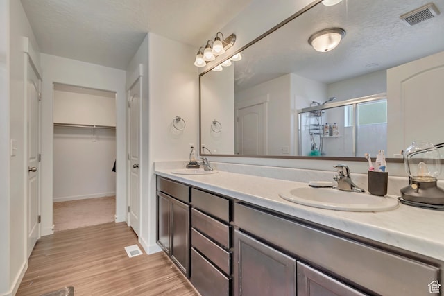 full bath with a stall shower, double vanity, wood finished floors, and baseboards