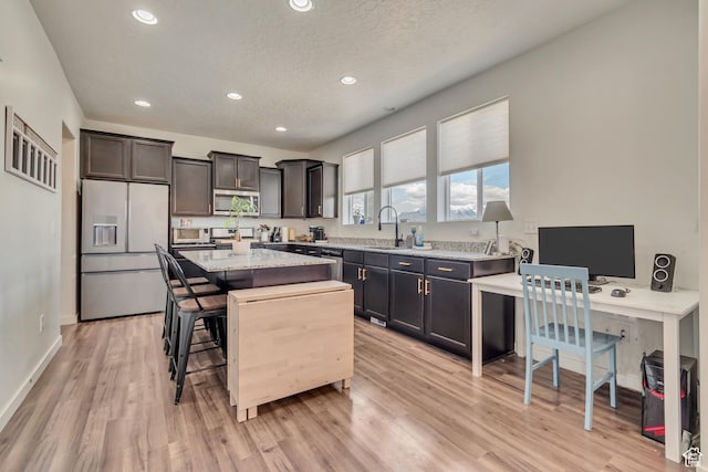 kitchen with appliances with stainless steel finishes, a sink, a center island, light wood-type flooring, and recessed lighting