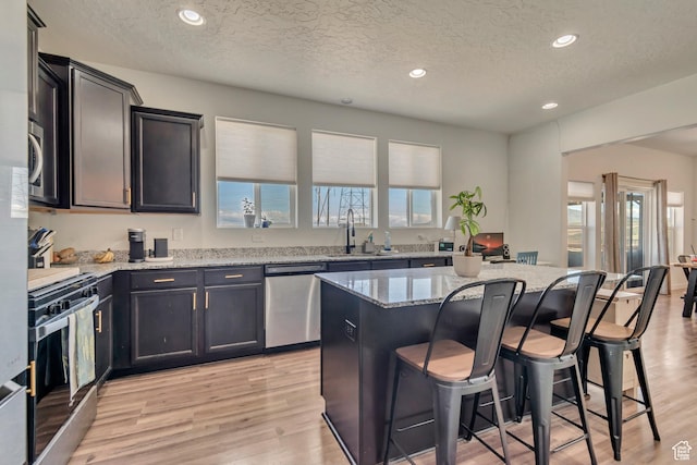 kitchen with appliances with stainless steel finishes, a sink, a textured ceiling, light stone counters, and a kitchen breakfast bar