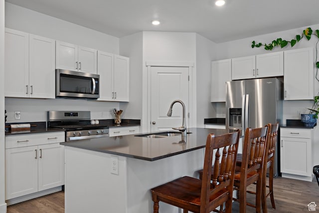 kitchen with stainless steel appliances, a sink, dark countertops, a breakfast bar, and dark wood-style flooring